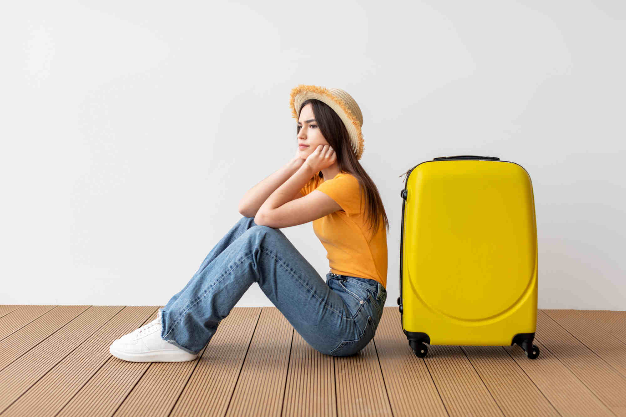 Una giovane donna seduta a terra accanto a una valigia gialla, con espressione pensierosa e postura stanca, trasmette un senso di ansia o incertezza legato al viaggio.