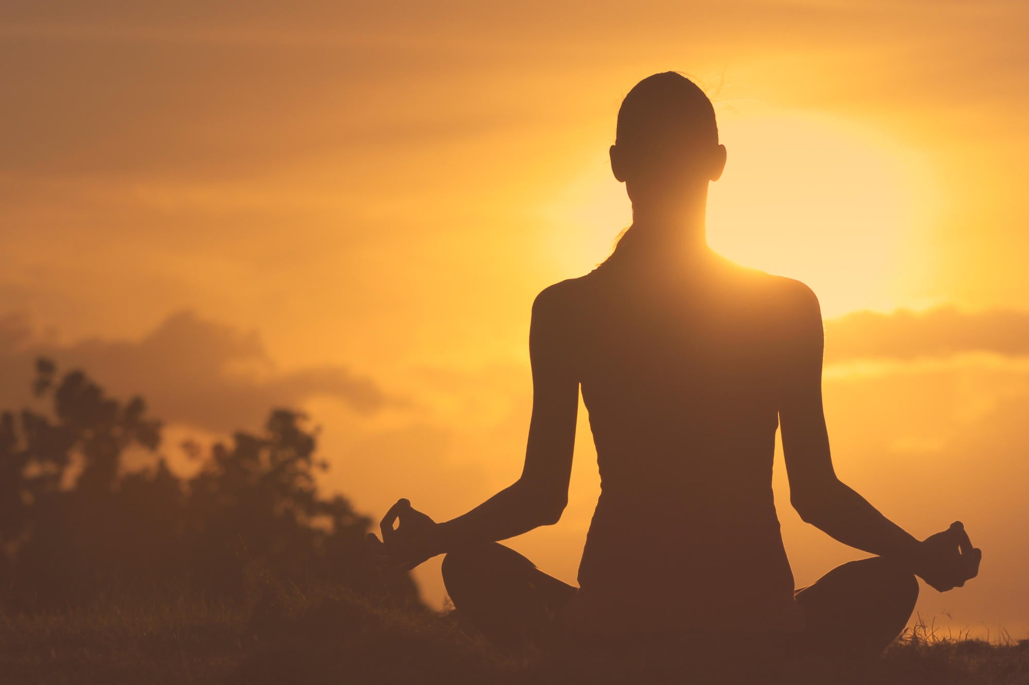Silhouette di donna che pratica tecniche di meditazione contro ansia e stress all'aperto, illuminata dalla luce del tramonto.